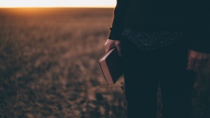 Une personne debout dans un champ, tenant une Bible et le soleil se couche