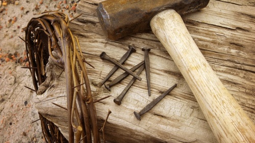 Illustration photo d'une couronne d'épines, de vieux clous, d'un marteau et d'une poutre en bois.