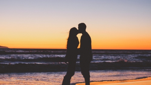 Un couple marié s'embrasse sur la plage devant un coucher du soleil