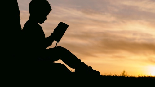 La silhouette d'un enfant qui lit la Bible devant un coucher de soleil en arrière-plan