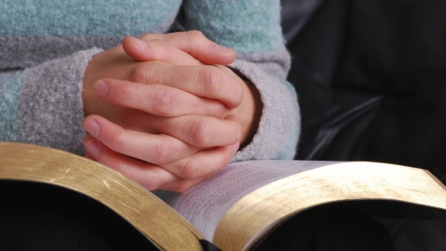 Une femme lit sa Bible avec des mains croisées en prière