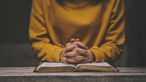 Une femme avec ses doigts croisés sur une Bible ouverte.