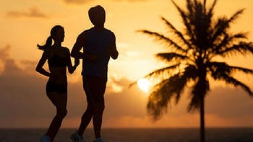 Homme et femme qui court sur la plage avec un palmier en arrière-plan.