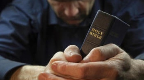 Un homme priant en tenant une Bible.