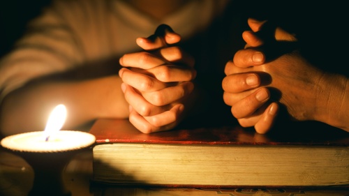 Prier avec les mains sur une Bible. Il y a une chandelle qui s'allume.