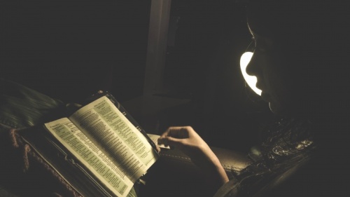 Une femme lit la Bible à la lumière d'une lampe