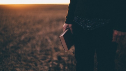 Une personne debout dans un champ, tenant une Bible et le soleil se couche