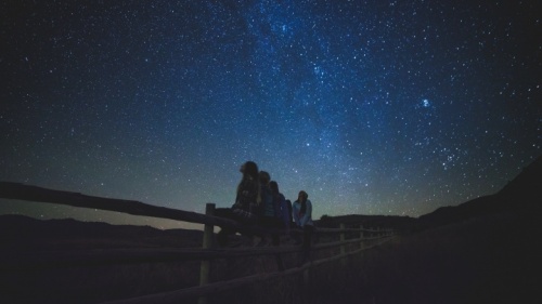 Un groupe de filles assises sur une clôture qui regardent les étoiles.