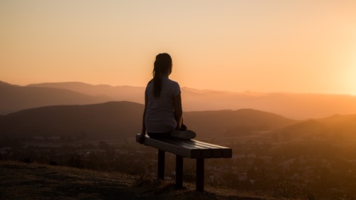 Une femme assise sur un banc regardant le coucher du soleil.