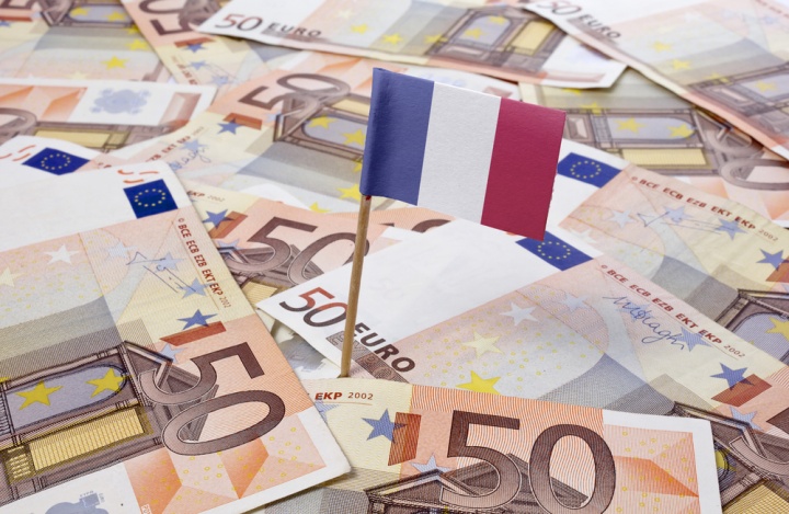 Un drapeau français trône sur une tapisserie de billets de banque en euros.