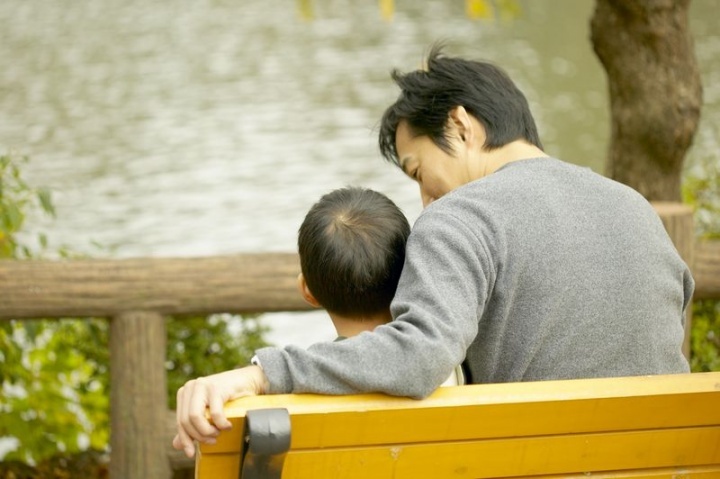 Un père et son fils s'assoient sur un banc au parc. Le père sourit en parlant à son fils.
