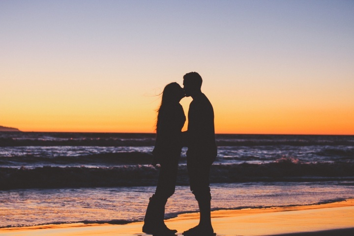 Un couple marié s'embrasse sur la plage devant un coucher du soleil