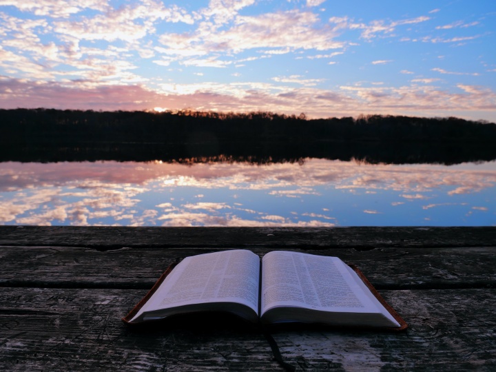 Une Bible avec le soleil qui se lève derrière des nuages sur un lac en arrière-plan