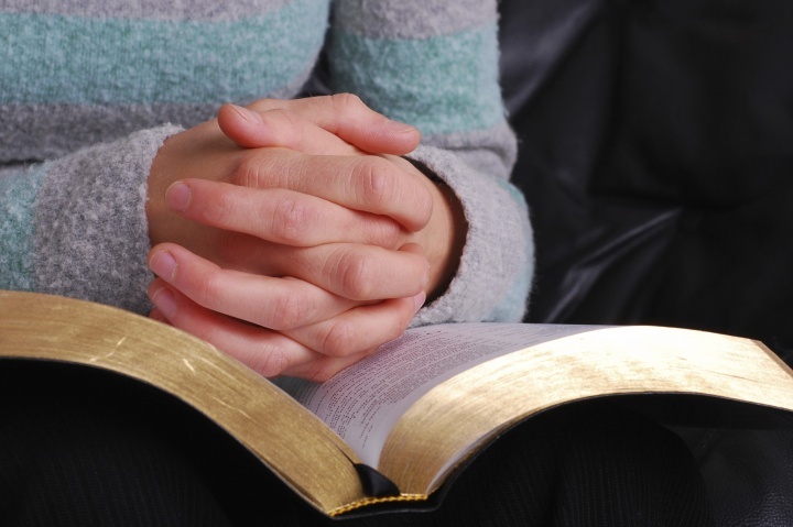 Une femme lit sa Bible avec des mains croisées en prière