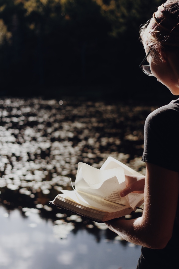 Une femme lit la Bible à côté d'un lac
