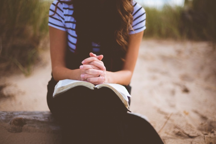Une femme sur la plage prie en lisant sa Bible