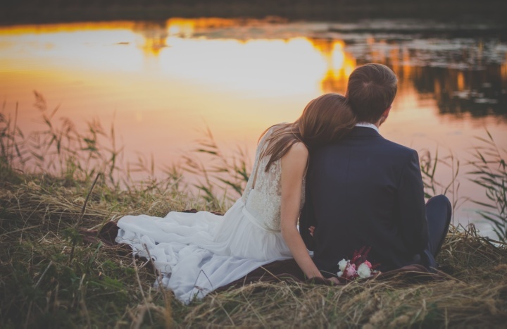 Un jeune couple marié sont assis au bord d'un lac au coucher du soleil