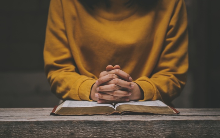 Une femme avec ses doigts croisés sur une Bible ouverte.
