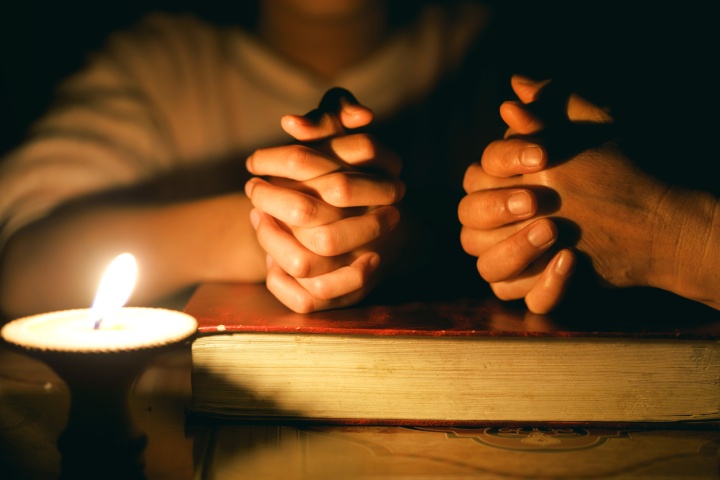 Prier avec les mains sur une Bible. Il y a une chandelle qui s'allume.