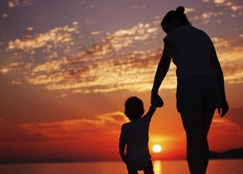 Une mère tenant la main de son enfant tout en regardant le coucher du soleil.