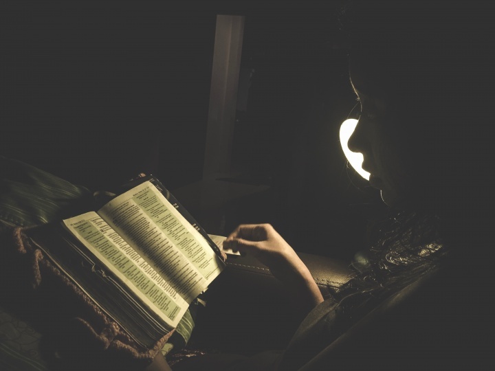 Une femme lit la Bible à la lumière d'une lampe