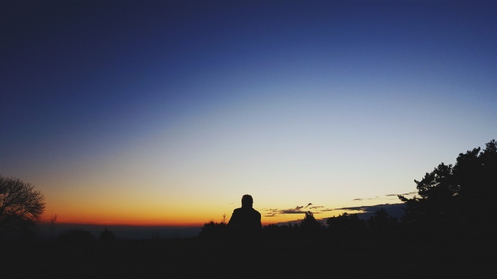 Une personne assise au sommet d'une colline regardant l'étendue du ciel nocturne.