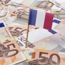 Un drapeau français trône sur une tapisserie de billets de banque en euros.