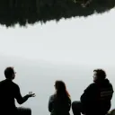 Trois personnes sont assis au bord d'un lac — une personne parle aux autres qui l'écoutent