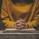 Une femme avec ses doigts croisés sur une Bible ouverte.