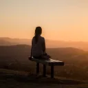 Une femme assise sur un banc regardant le coucher du soleil.