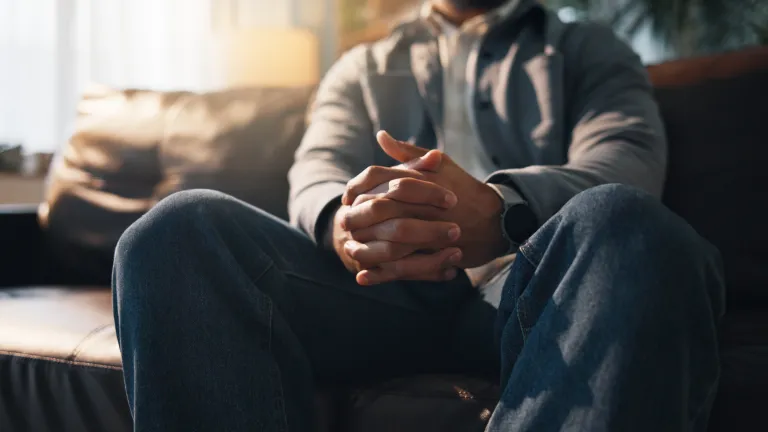 Anxiété, mains et thérapie avec une personne assise sur un canapé dans un cabinet pour un rendez-vous de consultation ou de counseling.