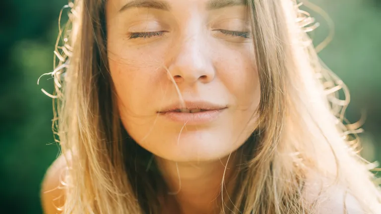 Portrait rapproché d’une femme aux yeux fermés, baignée par une chaude lumière naturelle du soleil