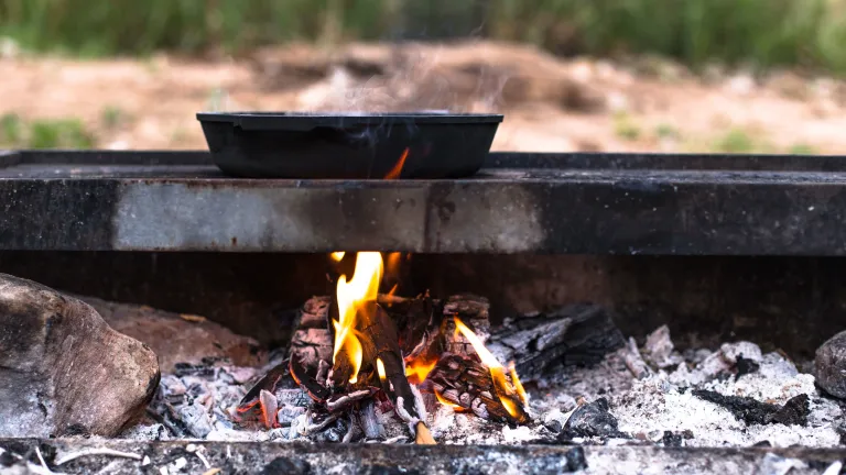 Une poêle en fonte posée sur une grille au-dessus d'un feu ardent.