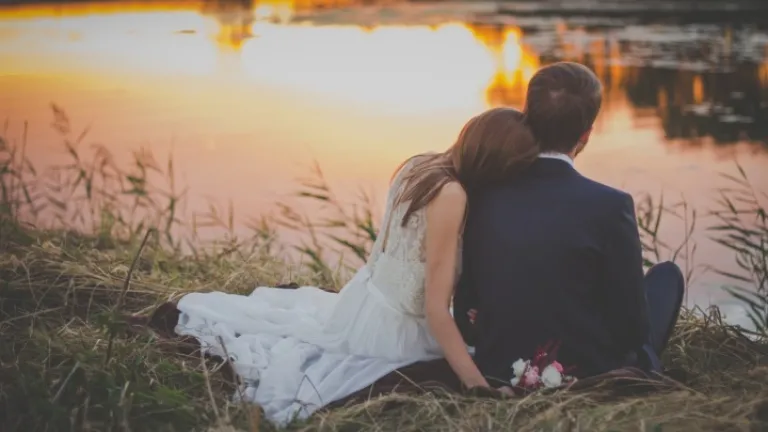 Un jeune couple marié sont assis au bord d'un lac au coucher du soleil