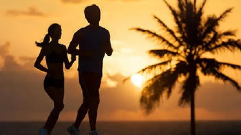 Homme et femme qui court sur la plage avec un palmier en arrière-plan.