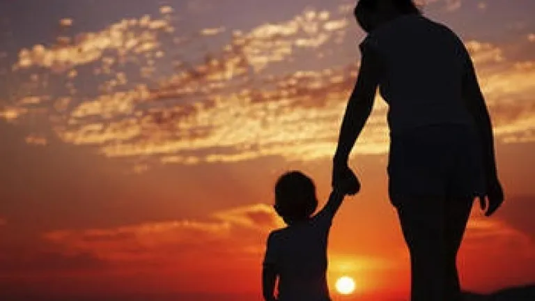 Une mère tenant la main de son enfant tout en regardant le coucher du soleil.