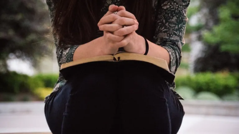 Une femme lit sa Bible avec des mains croisées en prière