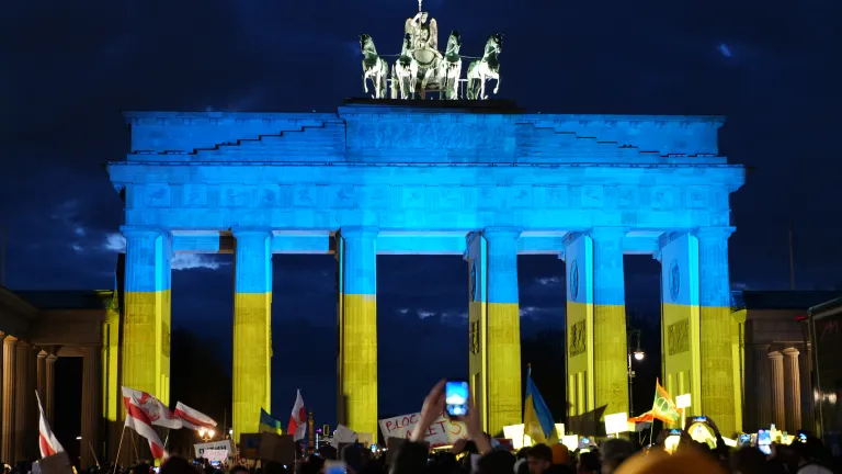 Des manifestants allemands témoignent leur solidarité avec l’Ukraine devant la célèbre porte de Brandebourg, illuminée aux couleurs du drapeau ukrainien.