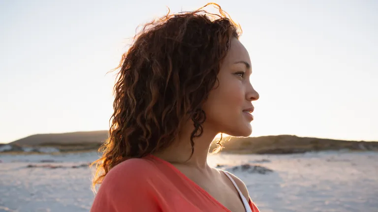 Vue latérale d'une belle femme métisse regardant au loin sur la plage