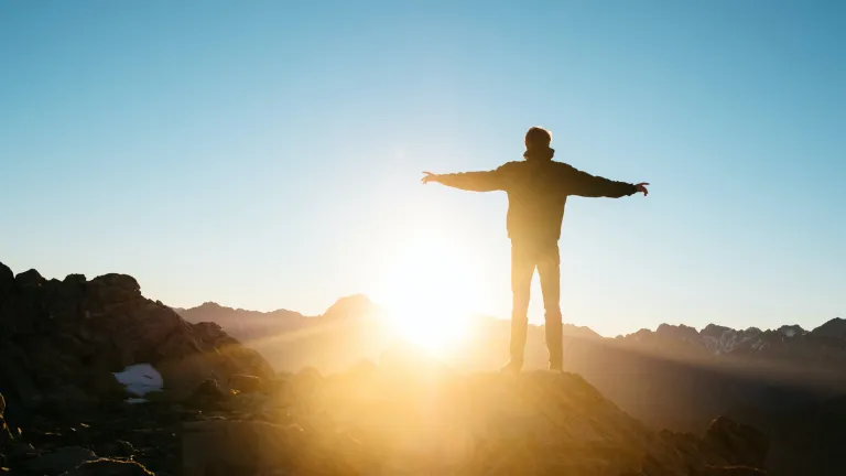 Un homme avec les bras écartés ; le soleil est devant lui.