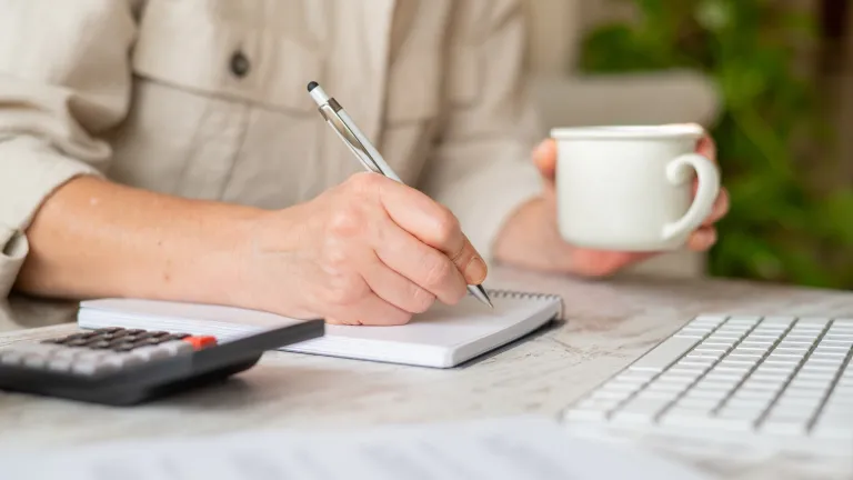 Femme se concentrant sur les finances personnelles, prenant des notes dans un cahier avec une calculatrice et une tasse de café