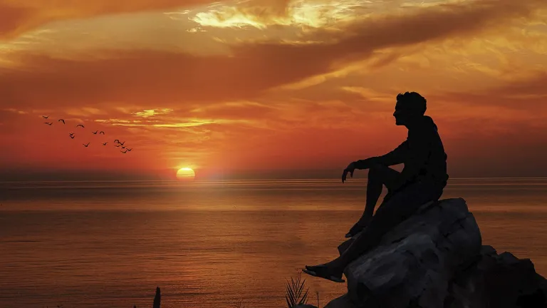 Homme assis sur un rocher regardant le coucher du soleil