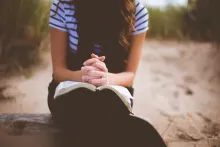 Une femme sur la plage prie en lisant sa Bible