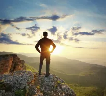 Un jeune homme sur une falaise en regardant le coucher du soleil.