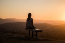 Une femme assise sur un banc regardant le coucher du soleil.