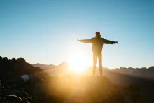 Un homme avec les bras écartés ; le soleil est devant lui.