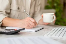 Femme se concentrant sur les finances personnelles, prenant des notes dans un cahier avec une calculatrice et une tasse de café 