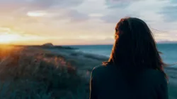 Une femme qui regarde au loin alors que le soleil se couche.