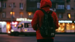 Une personne portant une veste et un sac à dos qui marche dans une ville.