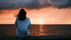 Une femme assise au bord de l’eau qui regarde le coucher du soleil.